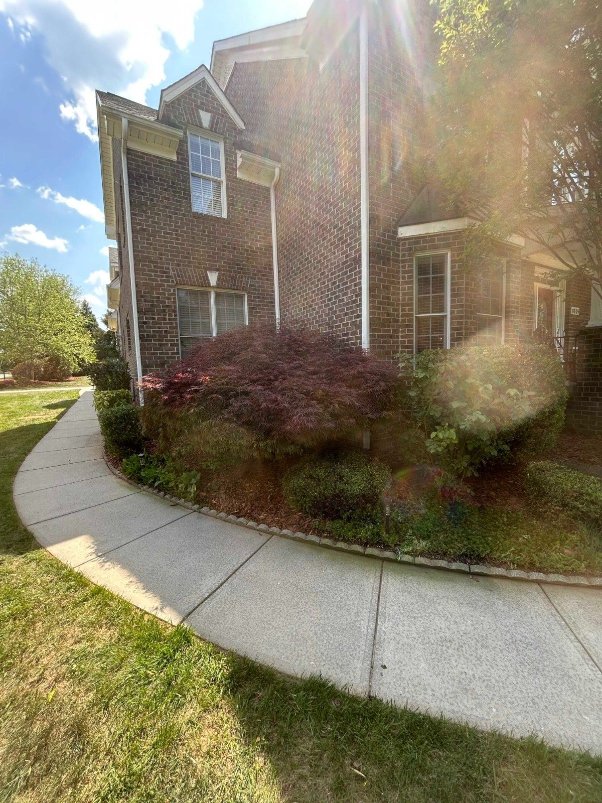 Brick house with a curved sidewalk, trimmed shrubs, and bright sun glare in front of the entrance