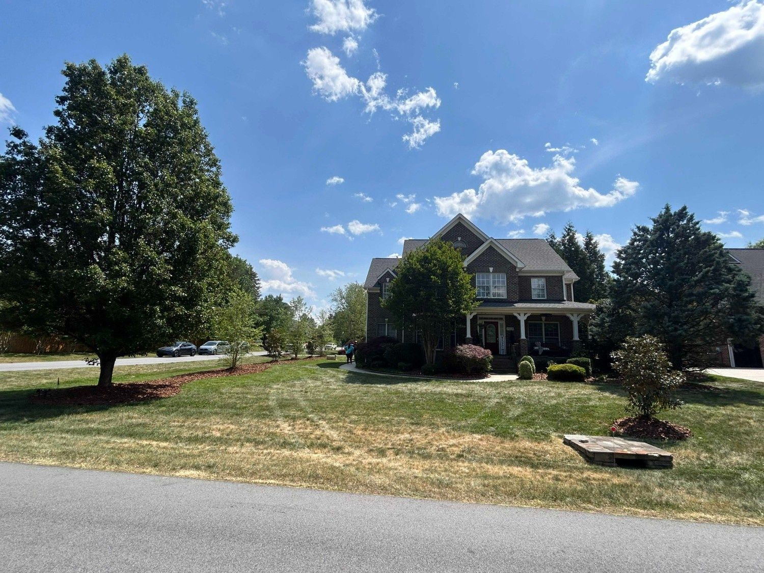 Suburban house with a large front lawn, trees, and a blue sky on a sunny day