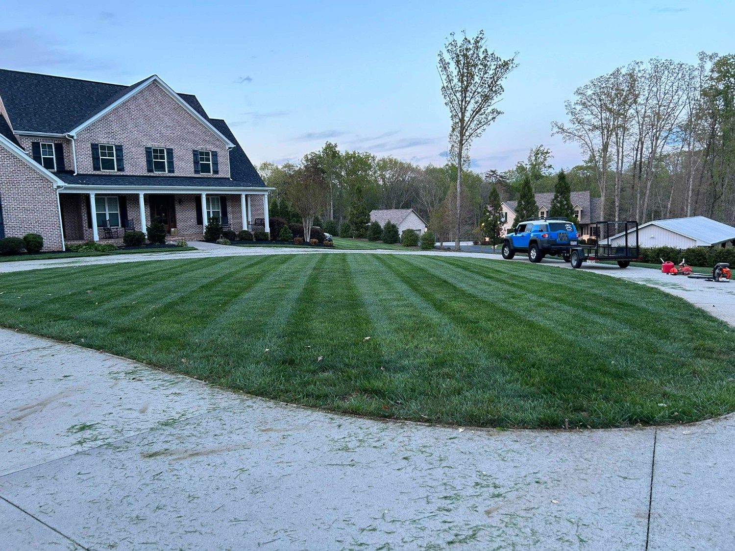 Large suburban house with a striped green lawn, a blue truck, and a gravel driveway at dusk