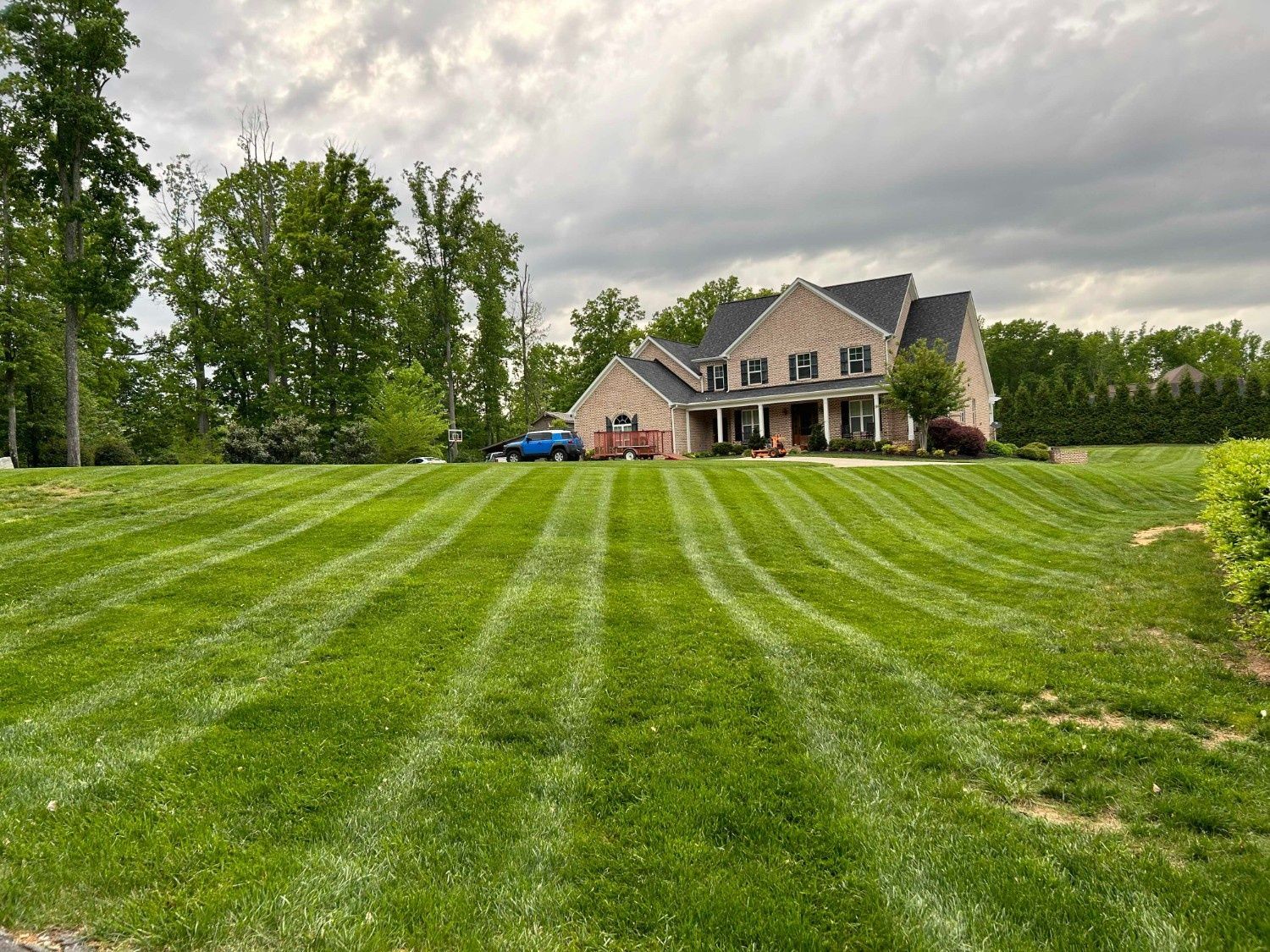 Large suburban house beyond a freshly mowed green lawn under a cloudy sky