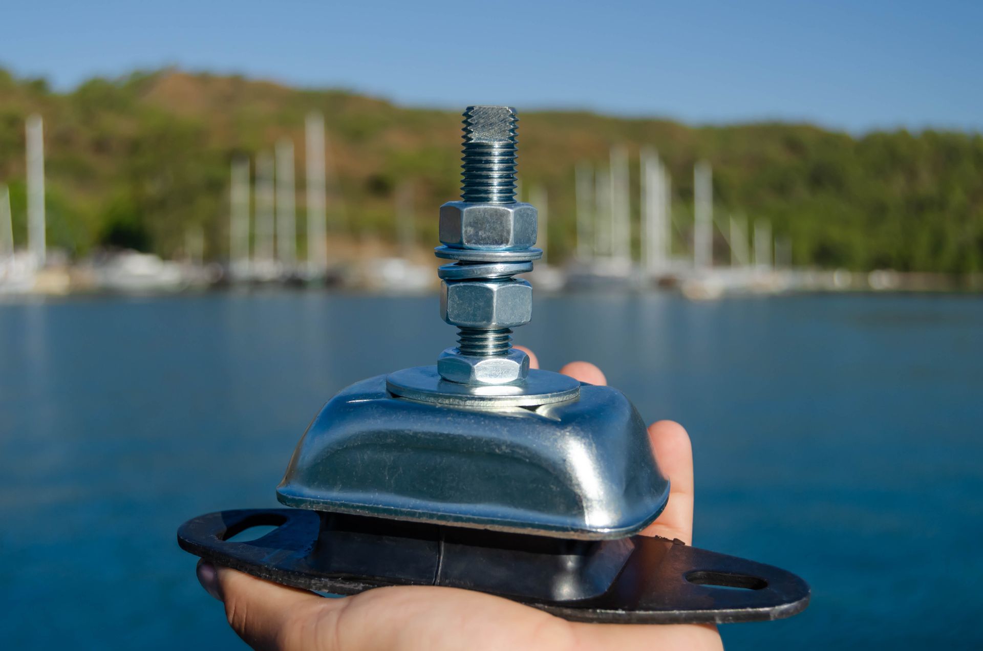 A close-up of a person holding a new marine engine mount for a sailing yacht in a marina.
