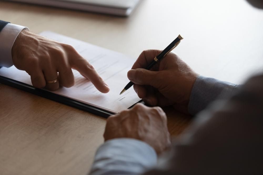 A Man is Signing a Document While Another Man Points at It — Tony Love Lawyers in Casino, NSW