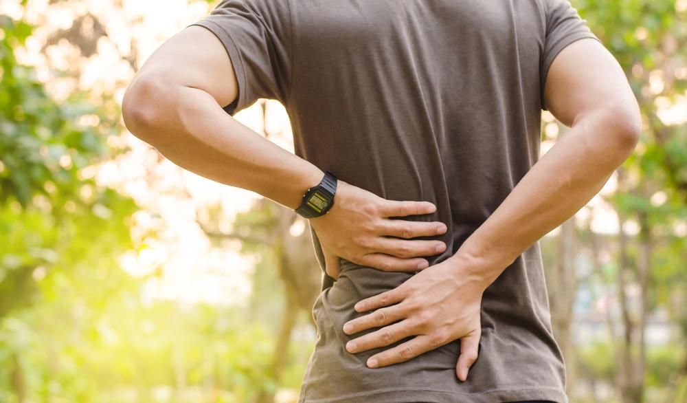 A Man is Holding His Back in Pain While Wearing a Watch — Tony Love Lawyers in Byron Bay, NSW