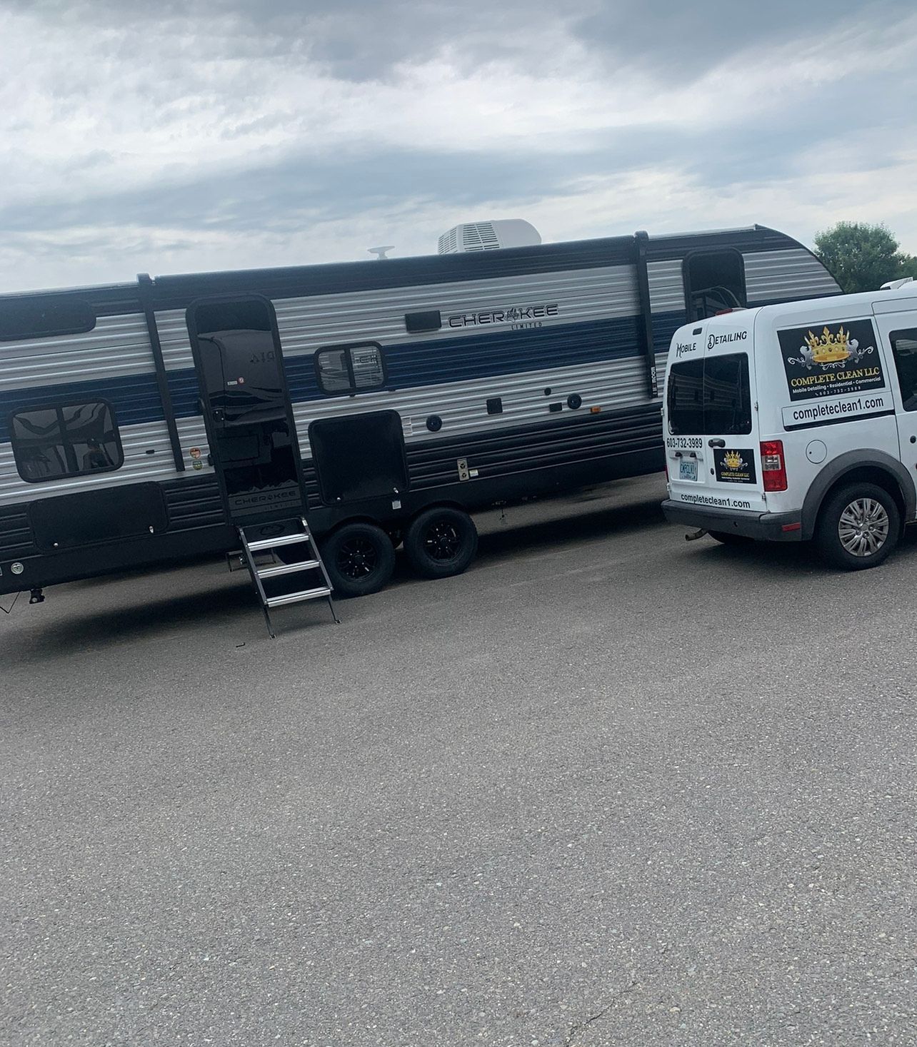 A large RV with a white van parked next to it, both on pavement under a cloudy sky.