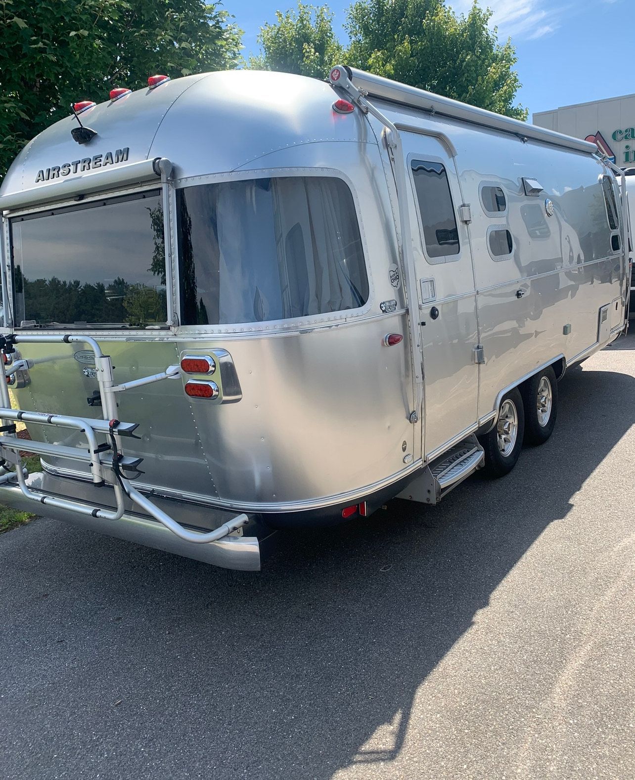 Silver Airstream trailer parked on pavement; a bike rack is attached to the back.