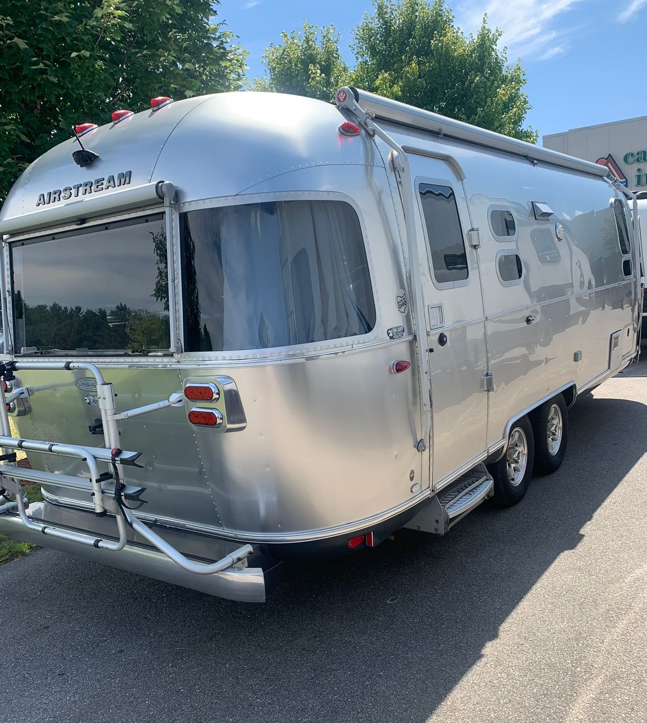 A shiny silver Airstream trailer with large windows and a rear bike rack, parked outside on a sunny day.