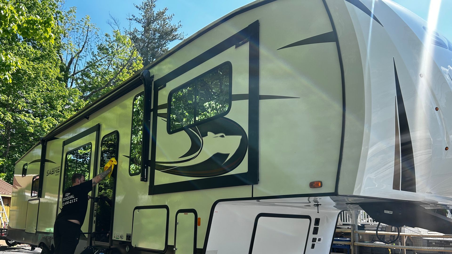 Person cleaning the exterior of a large, cream-colored RV parked outdoors.
