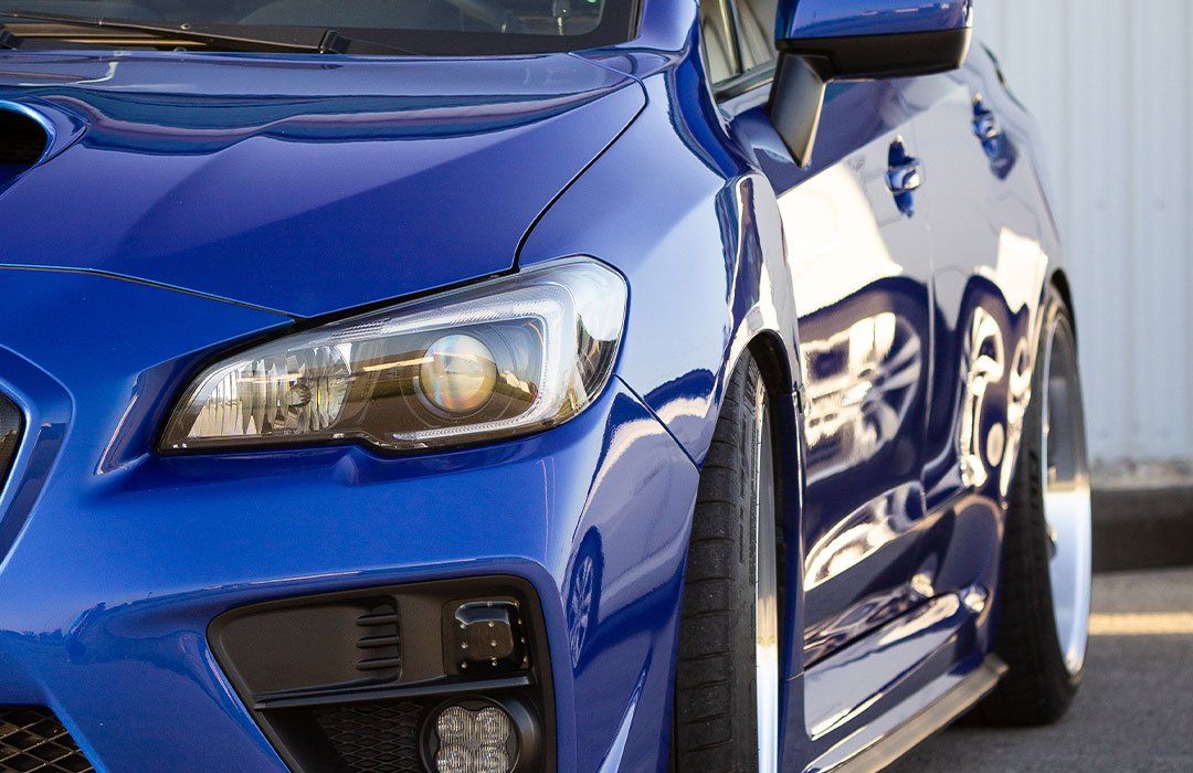 Blue Subaru car, close-up of front end; lowered suspension, angled wheels, chrome rims.