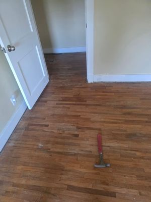 Empty room with wooden floor, open white door, and a hammer on the floor.