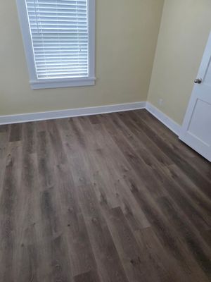 Empty beige room with wood-look flooring, a window with blinds, and a white closet door