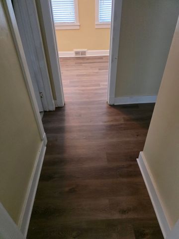 Narrow hallway with wood-look flooring and beige walls leading to a brighter room.