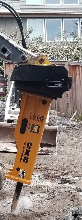 A yellow hydraulic hammer is attached to a bulldozer.