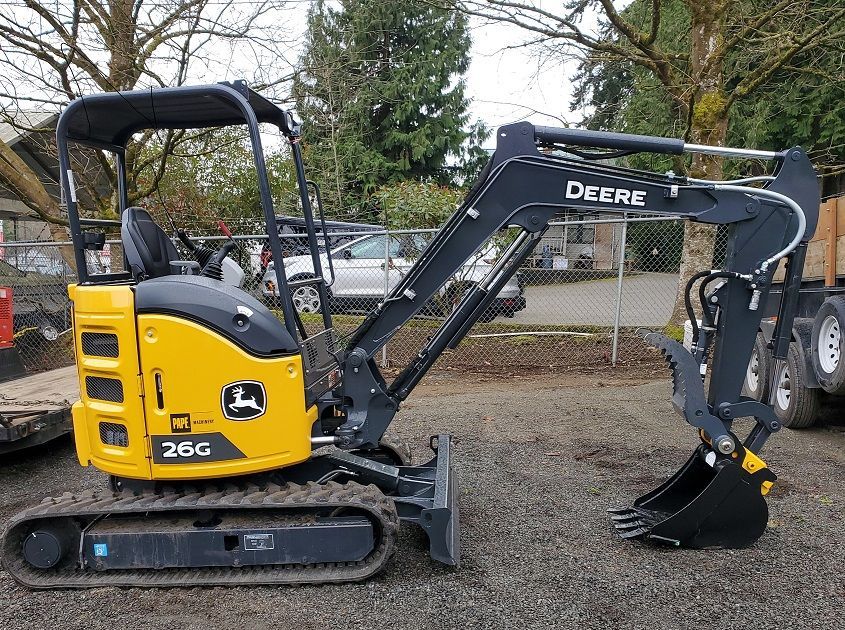 A small yellow and black excavator is parked in a gravel lot.