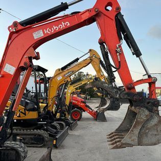 A row of construction vehicles including a red and yellow kubota excavator