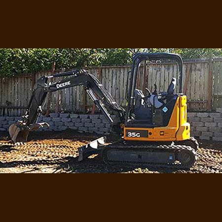 A small excavator is sitting in the dirt in front of a wooden fence.
