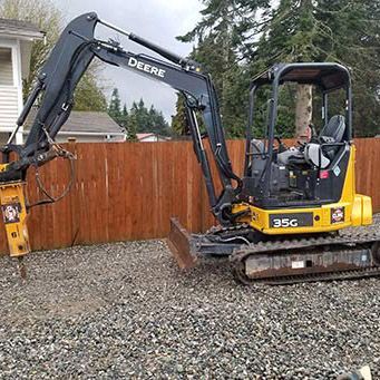 A small yellow excavator is parked in front of a wooden fence.