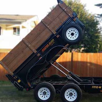 A dump truck with a wooden bed is parked in front of a wooden fence.