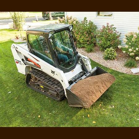 A bulldozer is sitting on top of a lush green lawn next to a house.
