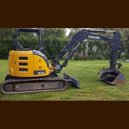 A small yellow and black excavator is parked in a grassy field.