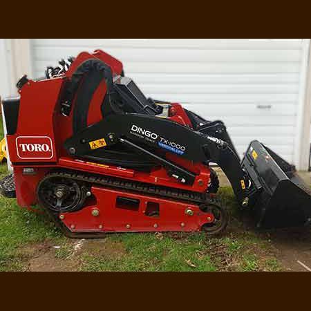 A red tractor with a black bucket is parked in front of a garage.