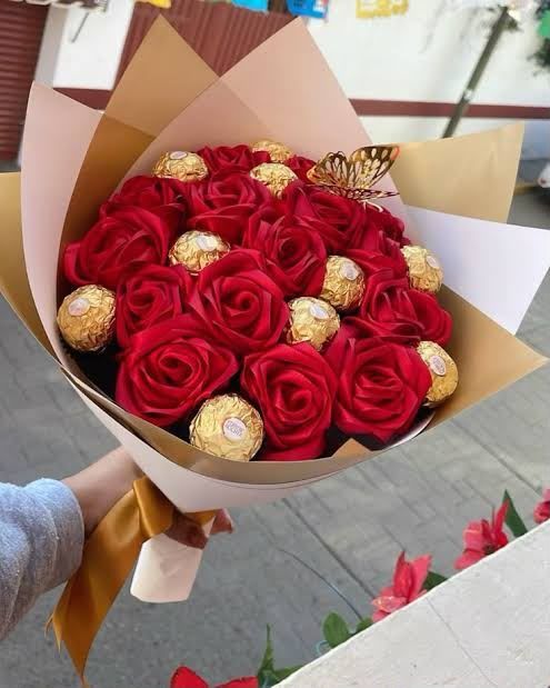 Ramo de rosas rojas envuelto en papel dorado y marrón, con bombones dorados entre las flores