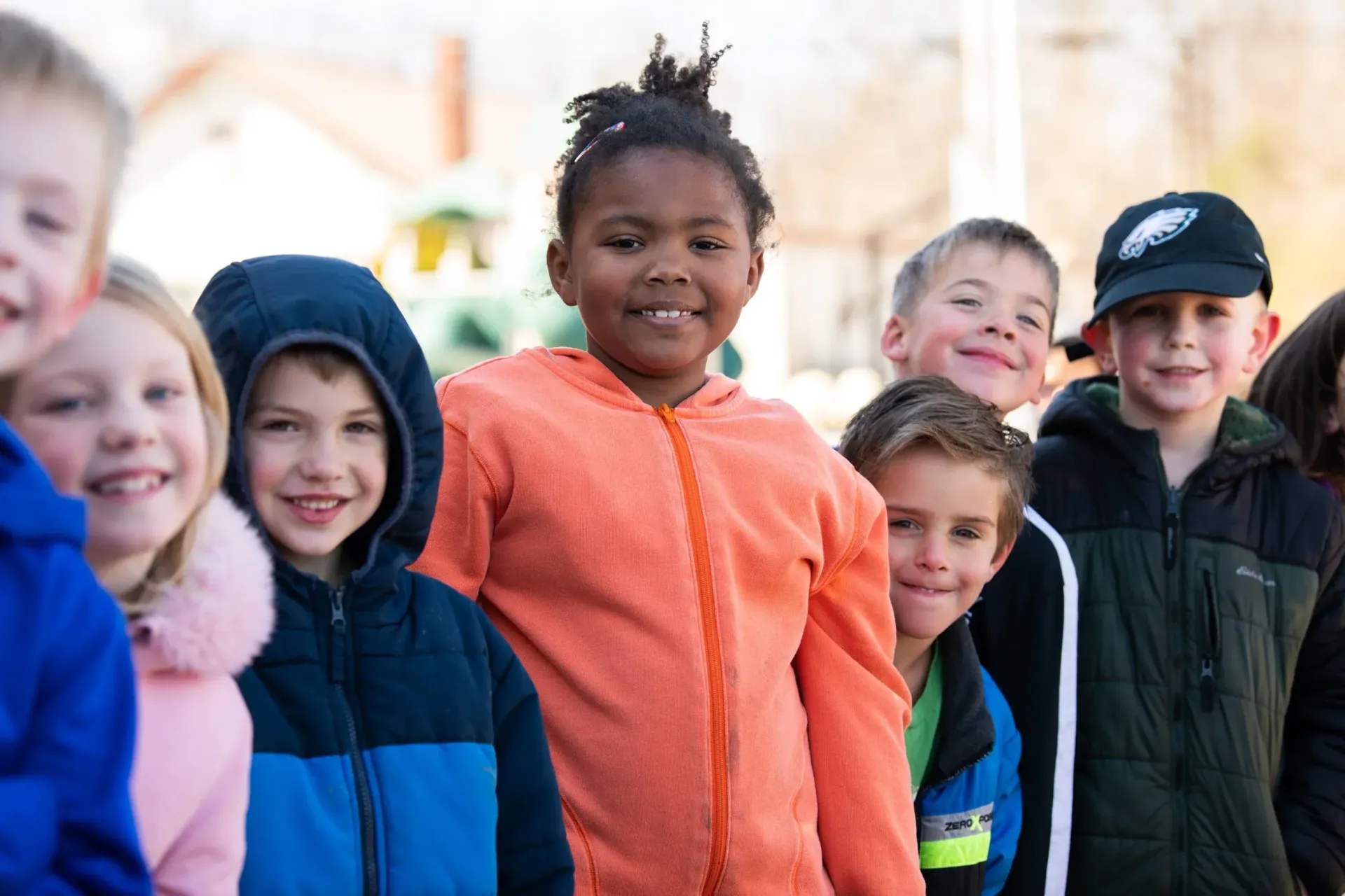 Group of smiling children outdoors, wearing jackets and hoodies.