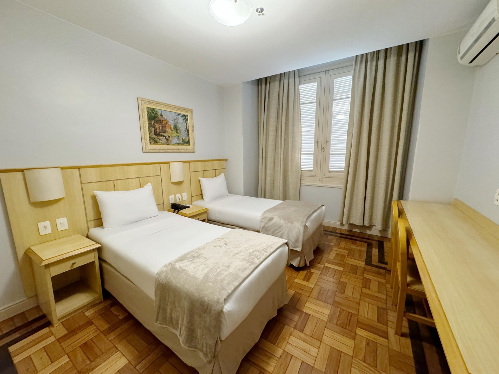 Um quarto de hotel com duas camas, uma escrivaninha e uma janela.