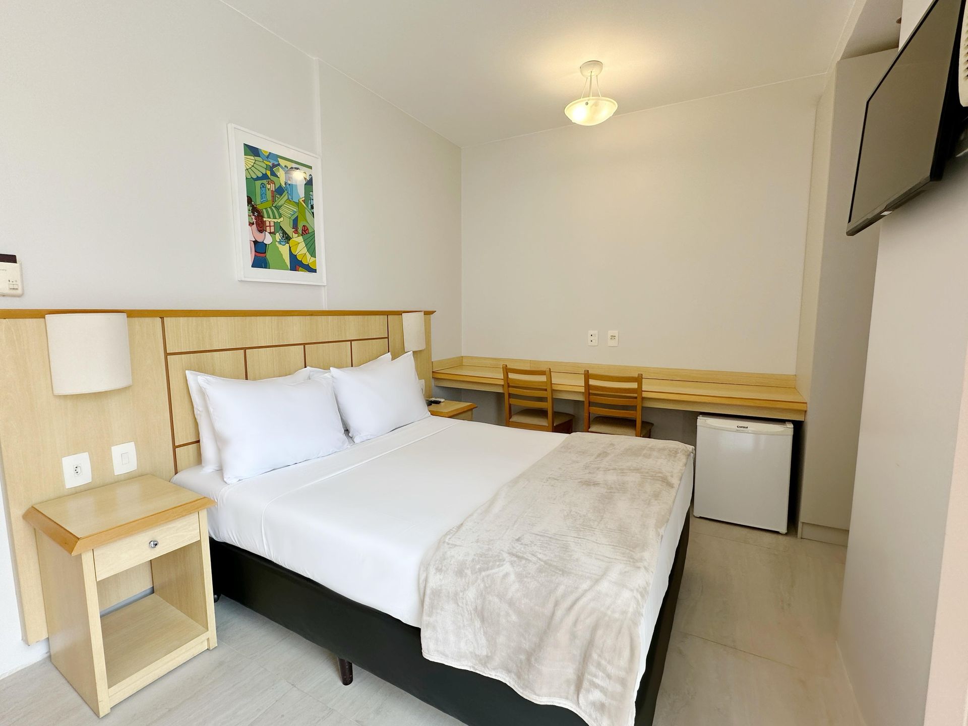Um quarto de hotel com uma cama king size, escrivaninha e cadeiras.