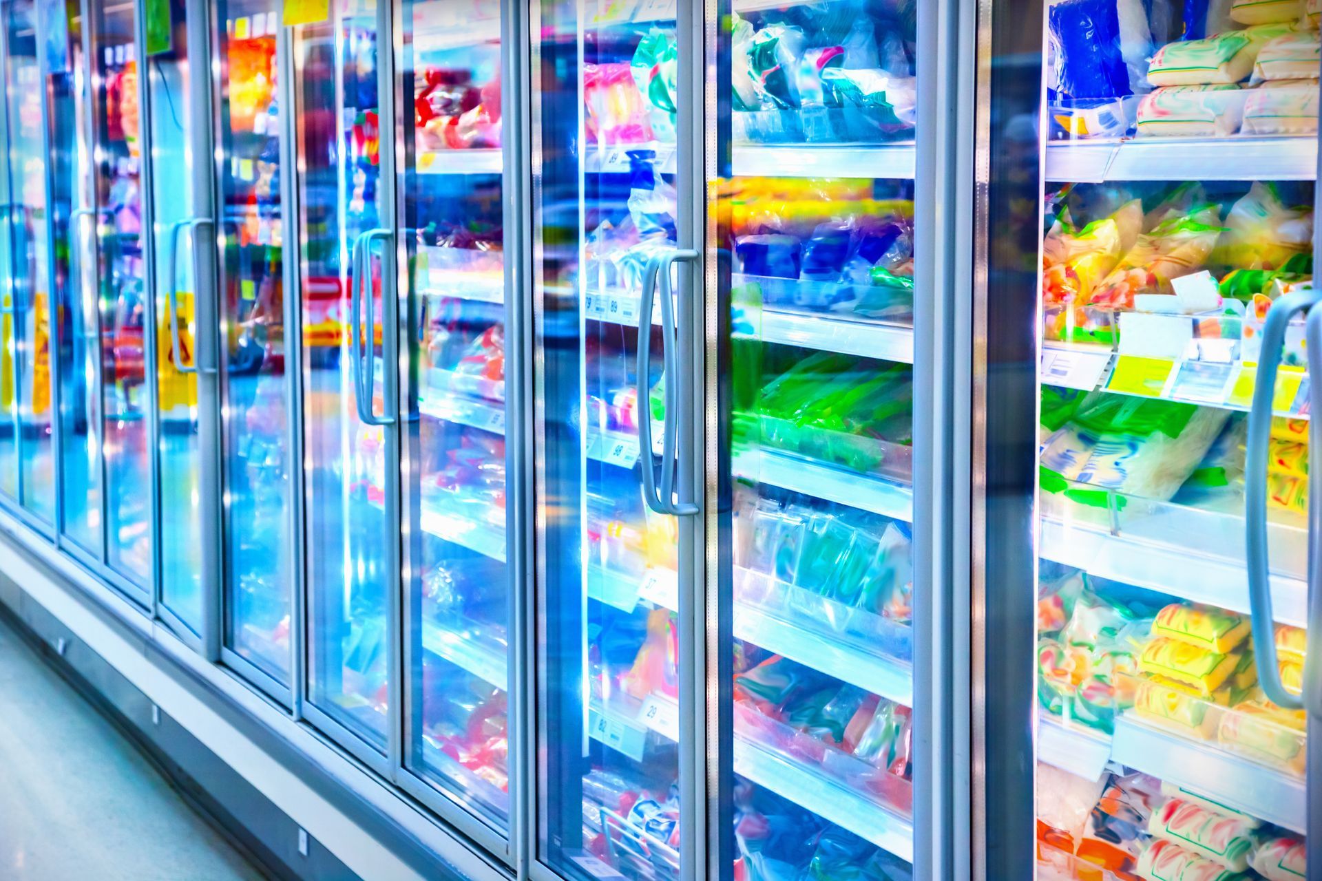 A row of brightly lit supermarket freezer doors with colorful packaged foods inside A row of brightly lit supermarket freezer doors with colorful packaged foods inside
