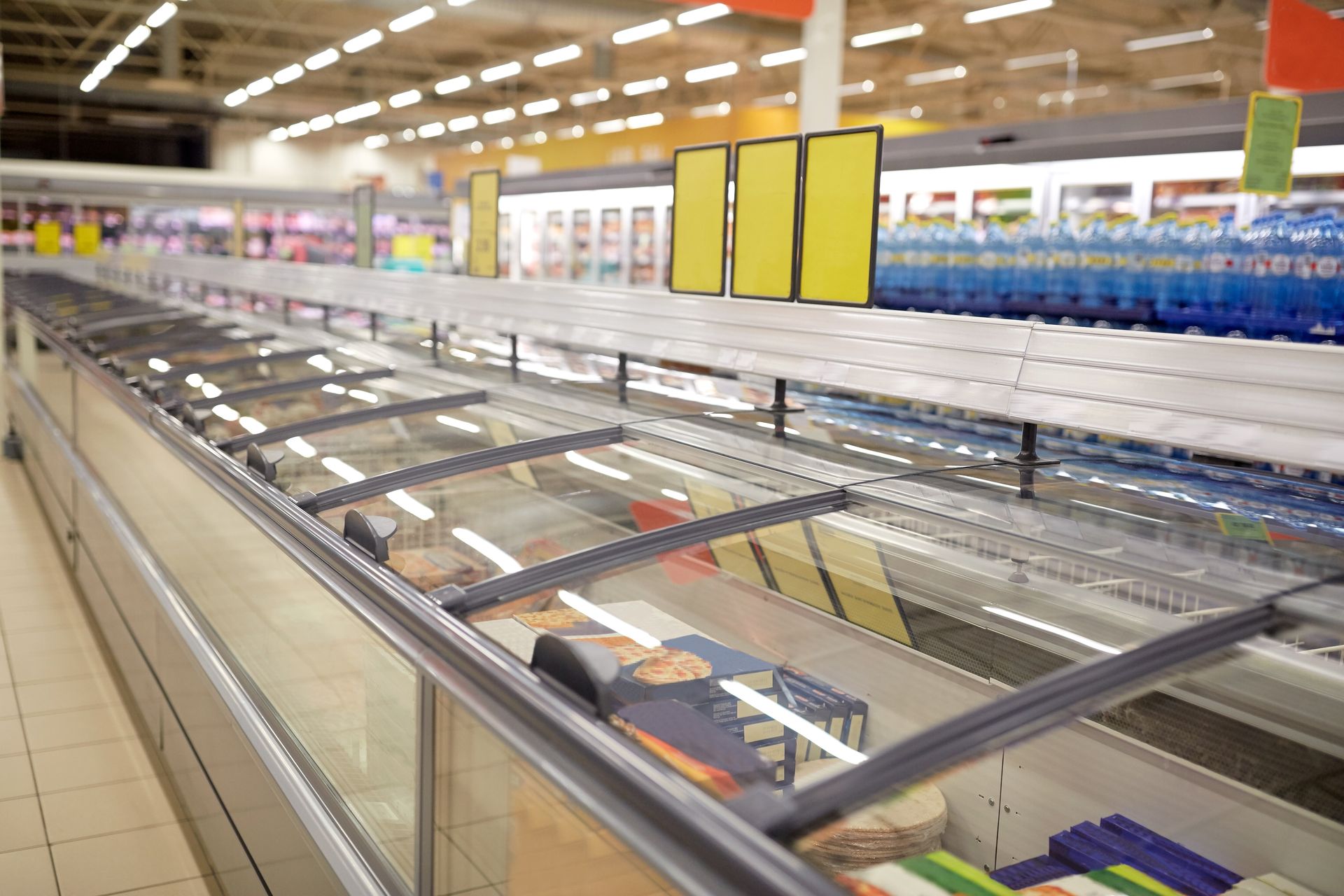 Empty supermarket freezer aisle with glass-top frozen food cases and yellow sale signs Empty supermarket freezer aisle with glass-top frozen food cases and yellow sale signs