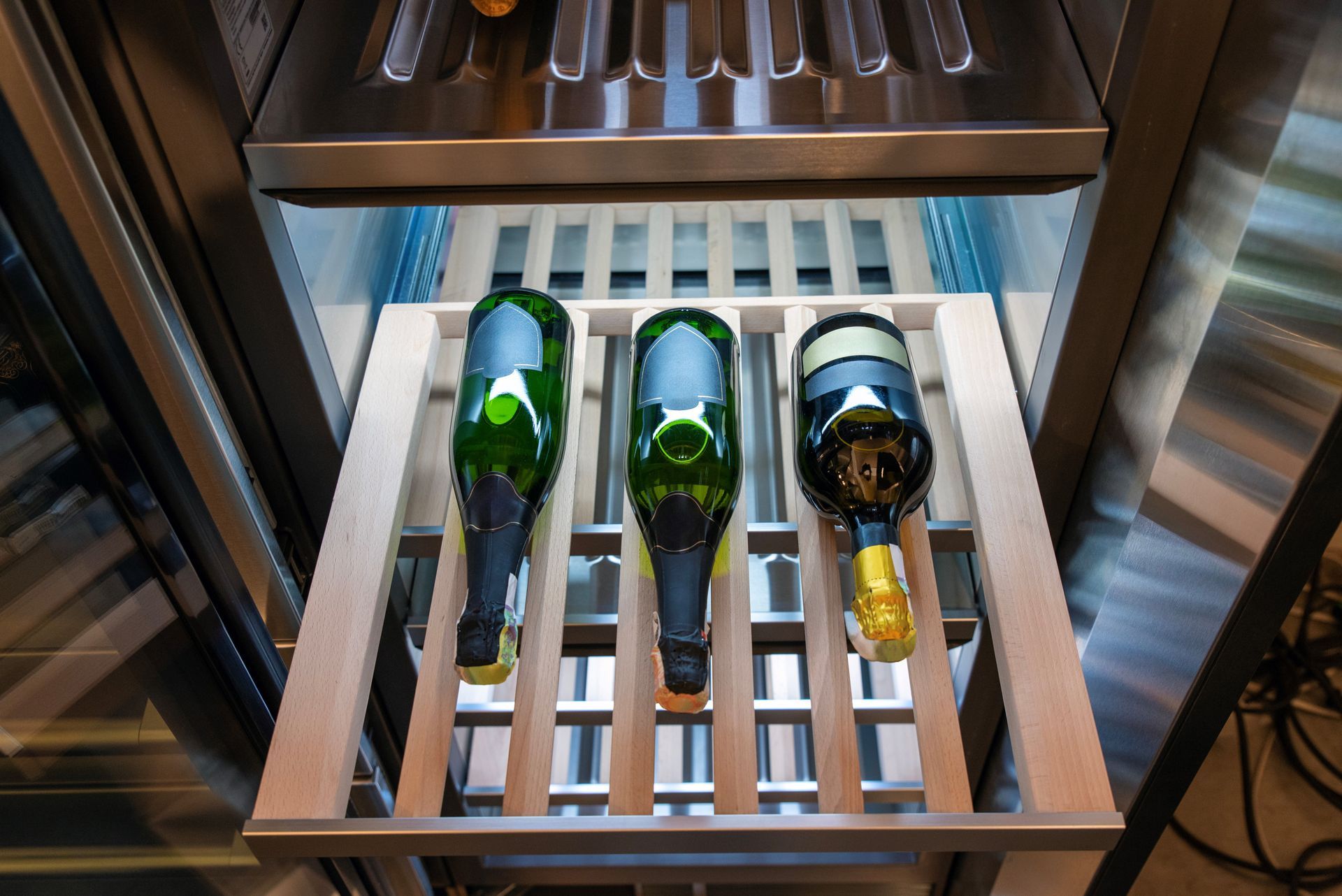 Three wine bottles lying on wooden racks inside a metal wine cooler Three wine bottles lying on wooden racks inside a metal wine cooler