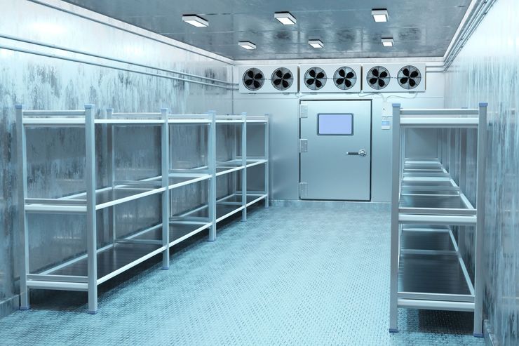 Sterile cold-storage room with metal shelves, fans, and a closed door under bright lights Sterile cold-storage room with metal shelves, fans, and a closed door under bright lights