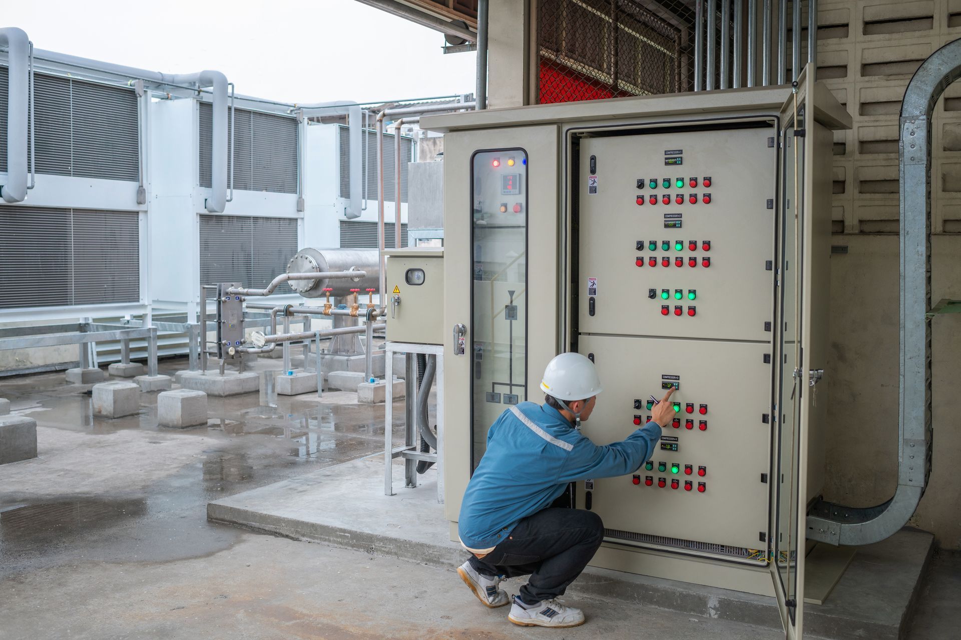 Worker crouches at an electrical control panel in an industrial facility. Worker crouches at an electrical control panel in an industrial facility.
