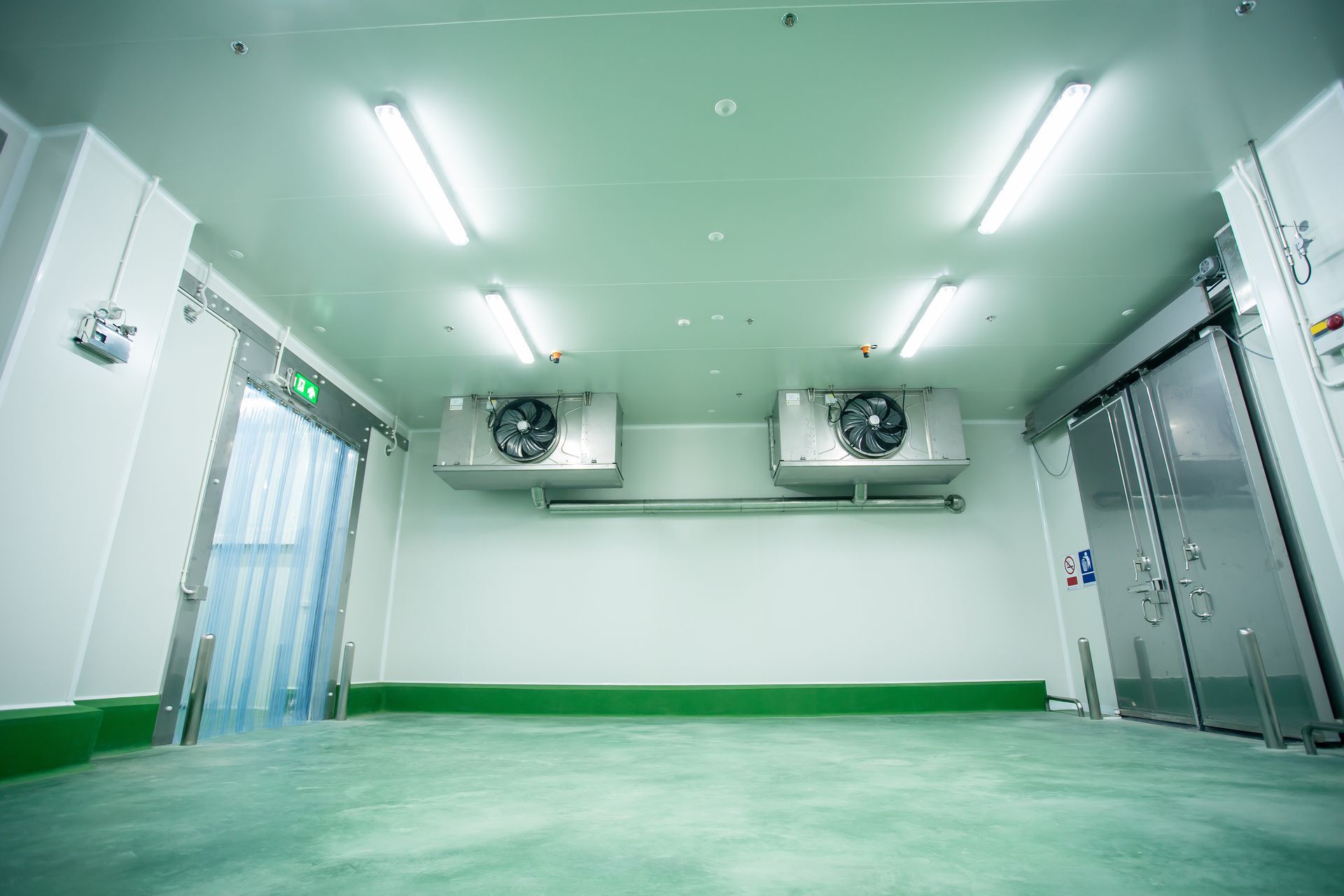 Empty sterile room with green floor, white walls, ceiling lights, and ventilation units over metal doors Empty sterile room with green floor, white walls, ceiling lights, and ventilation units over metal doors