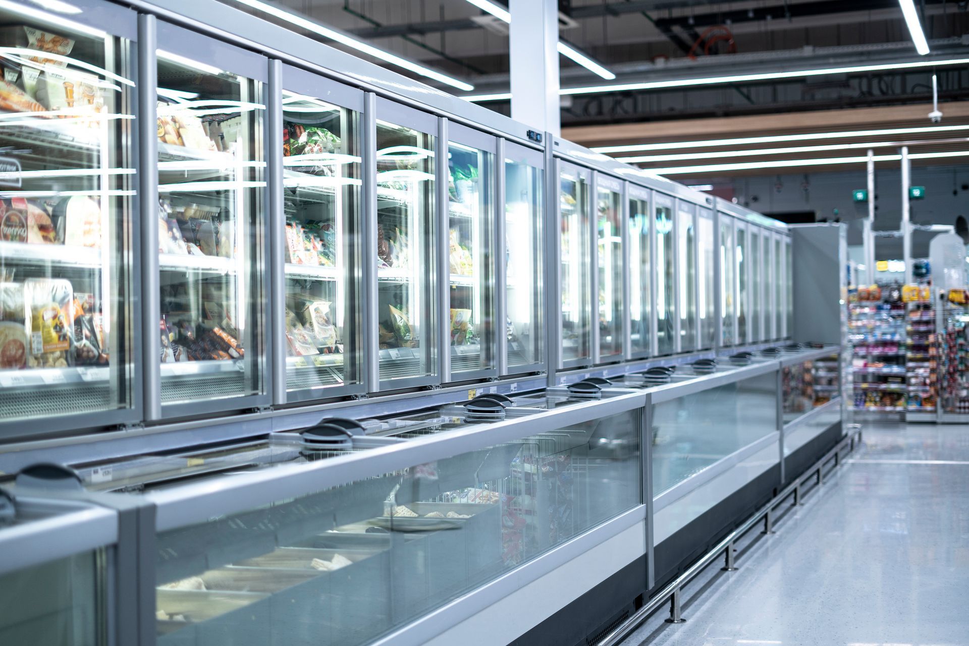 Empty supermarket frozen food aisle with glass-door freezers and bright overhead lights Empty supermarket frozen food aisle with glass-door freezers and bright overhead lights
