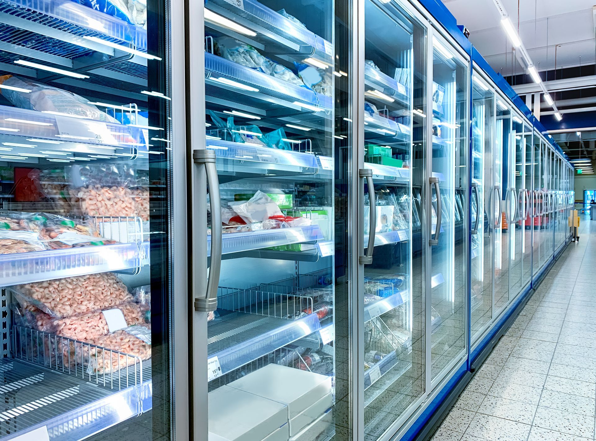 Frozen food aisles in a bright grocery store, with glass-door freezers lined along the corridor Frozen food aisles in a bright grocery store, with glass-door freezers lined along the corridor
