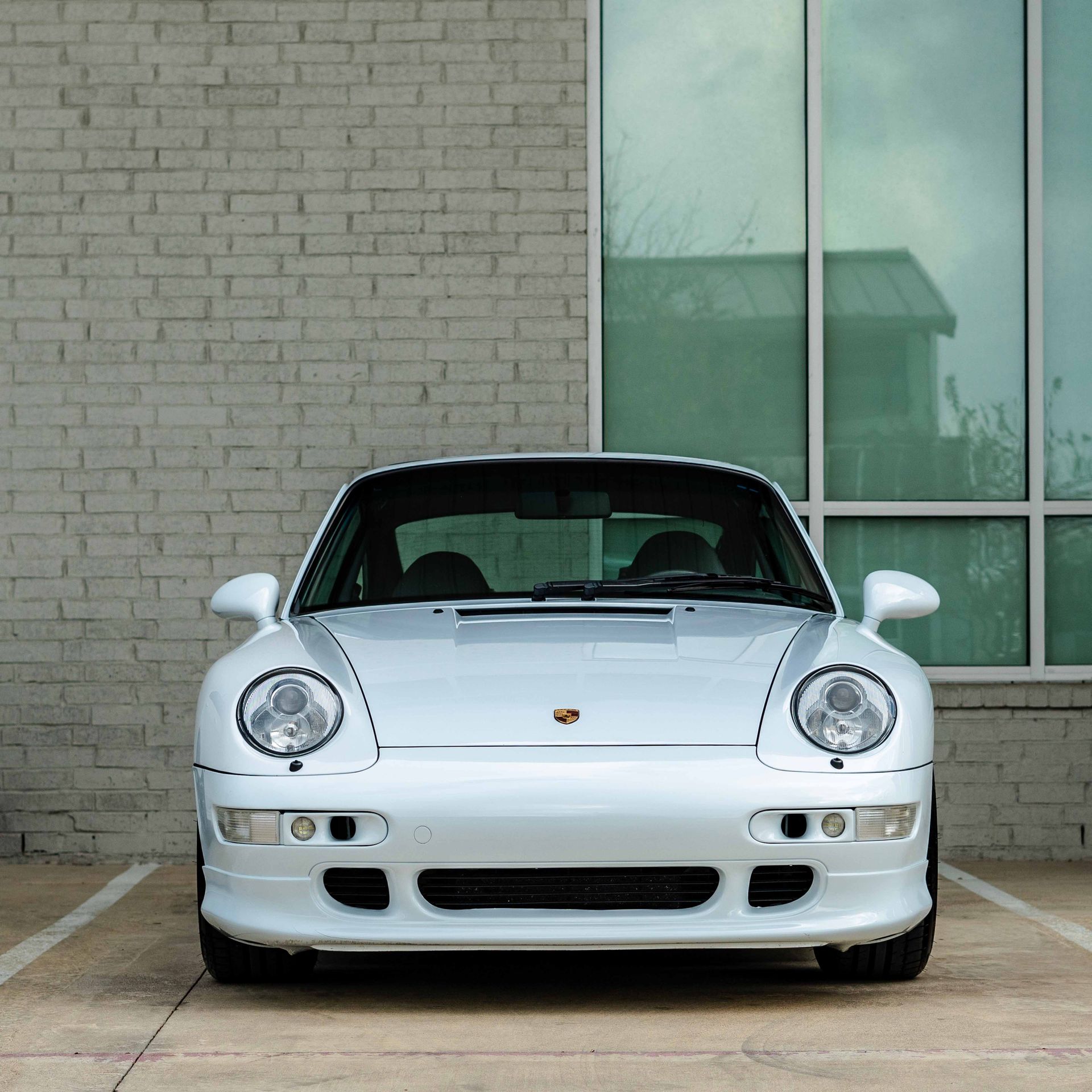Silver Porsche 911 parked in front of a brick building with large windows.