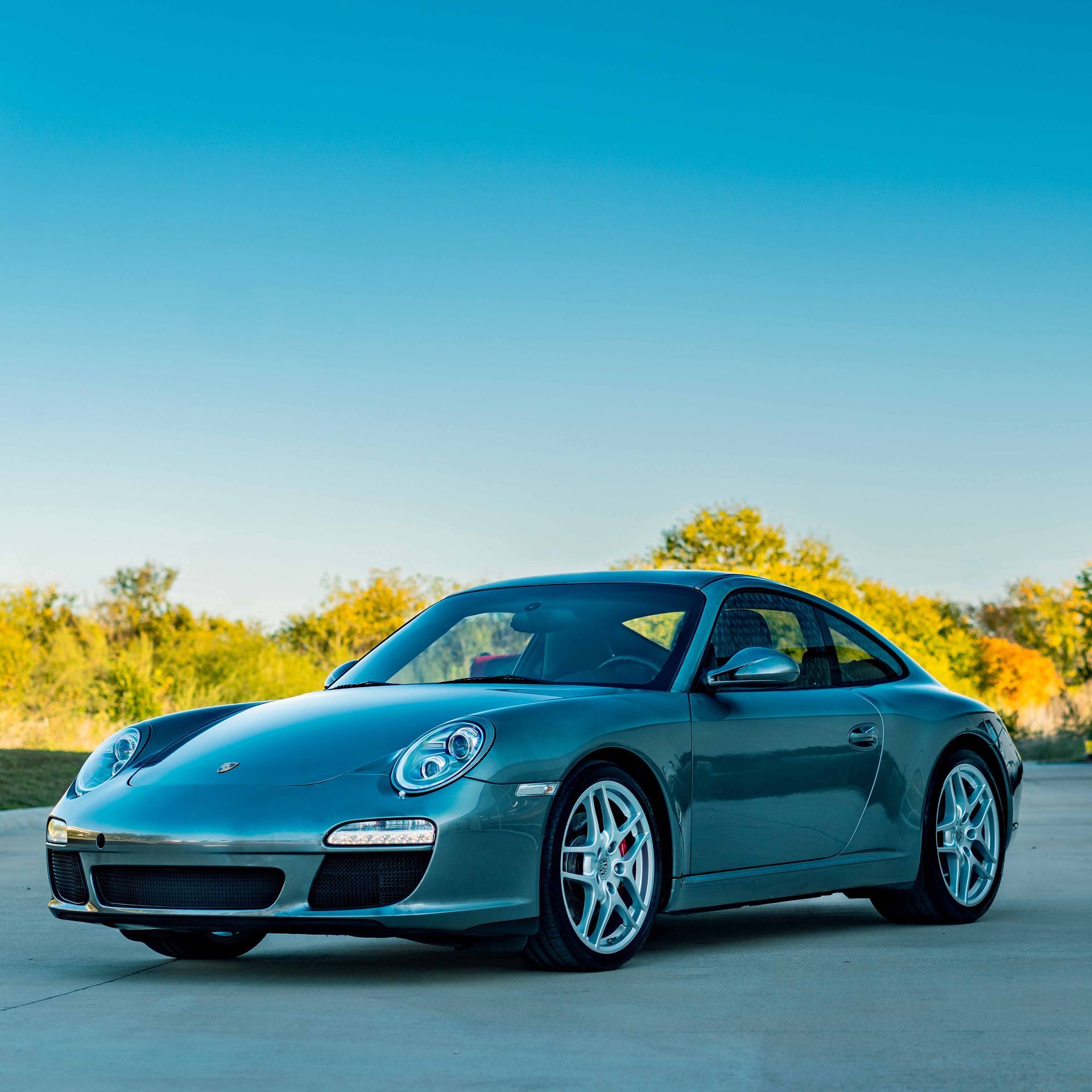 Gray Porsche coupe parked on pavement under a blue sky.