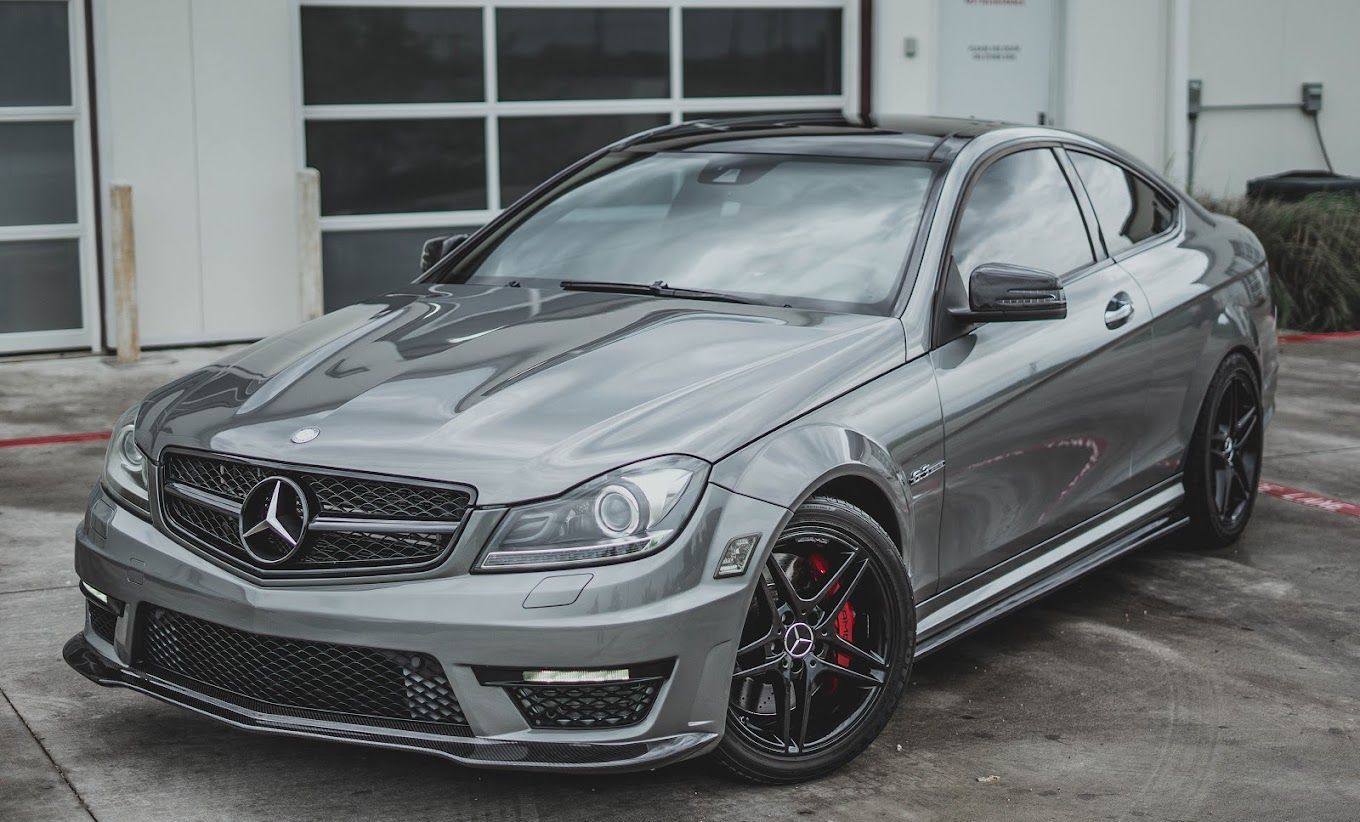 A mercedes benz c63 amg coupe is parked in a parking lot in front of a garage.