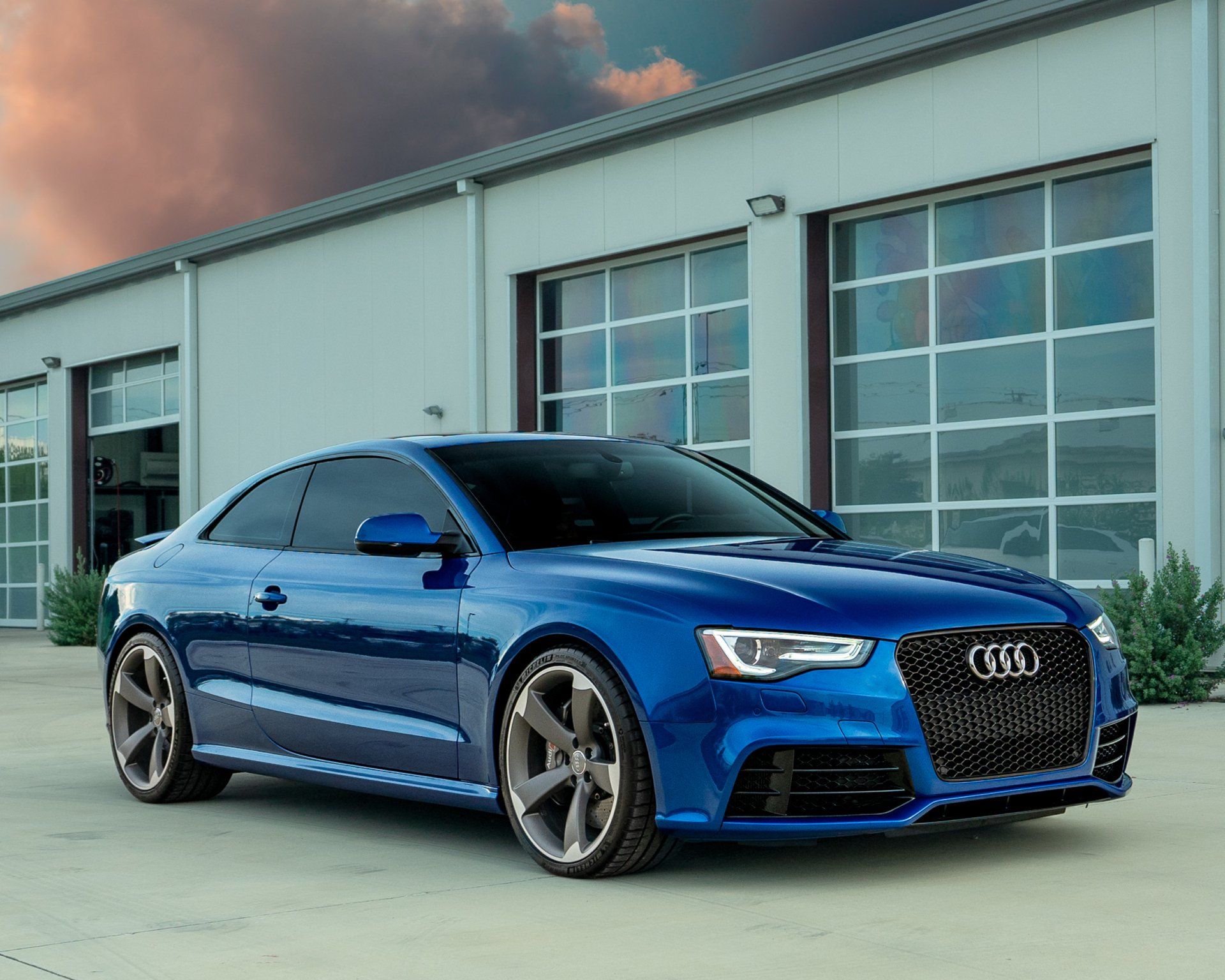 Blue Audi coupe parked outside a building with garage doors.