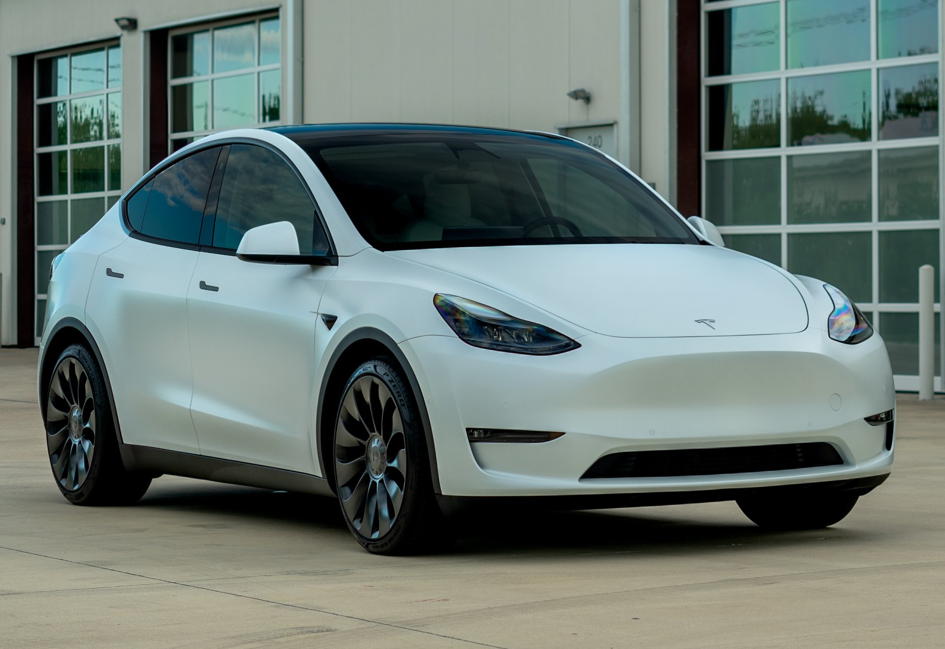 A white tesla model y is parked in front of a garage door.