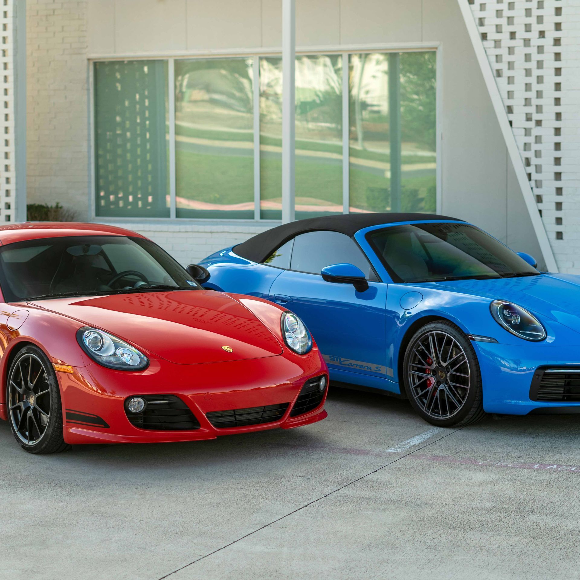 Red Porsche sports car next to a blue convertible Porsche, parked outside a building.