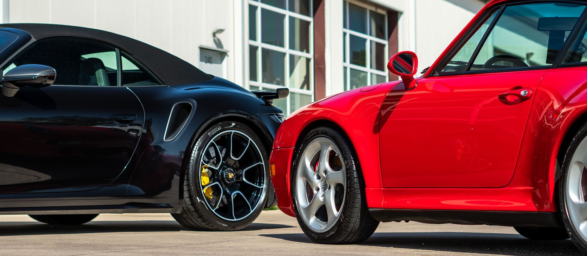 Two sports cars are parked next to each other in front of a garage.