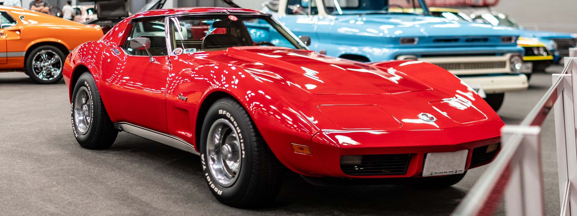 A red corvette is parked next to a blue truck at a car show.