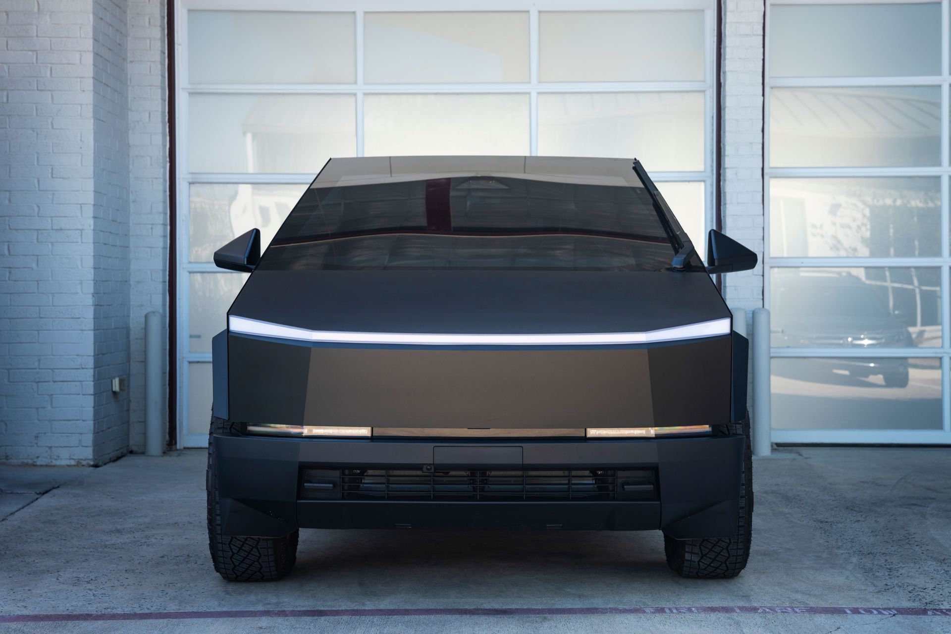 Matte black Tesla Cybertruck parked in front of a white garage door.