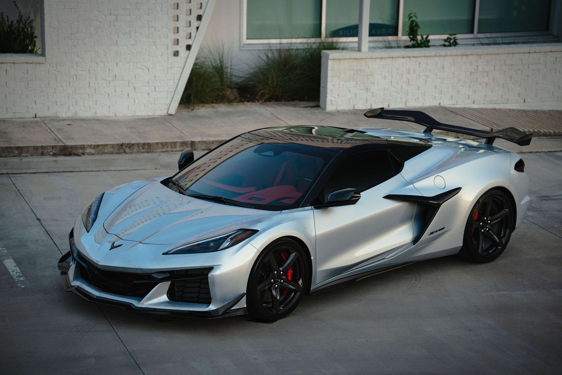 Silver Chevrolet Corvette sports car with black accents and spoiler, parked outside.