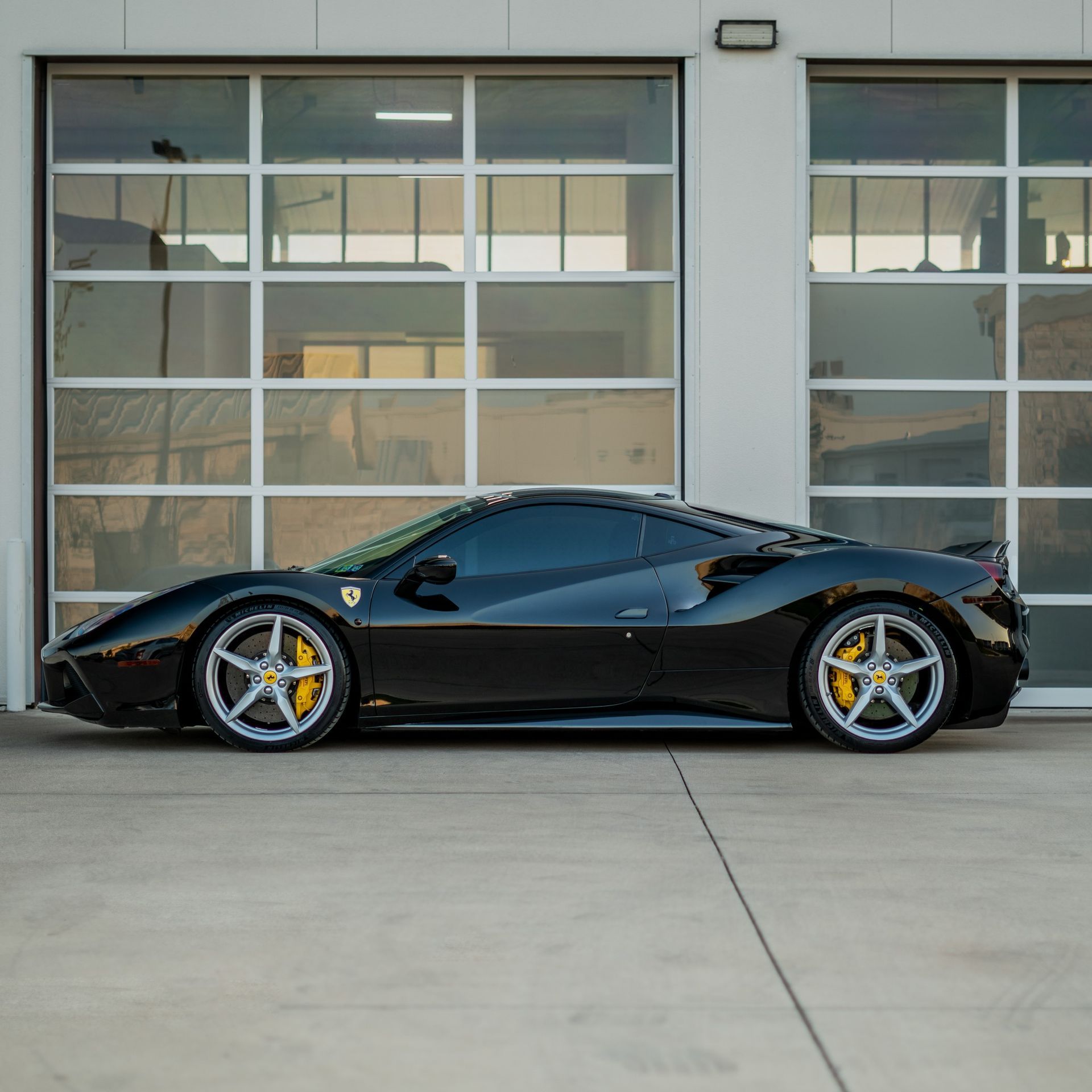 Black Ferrari sports car parked in front of a building with glass garage doors.