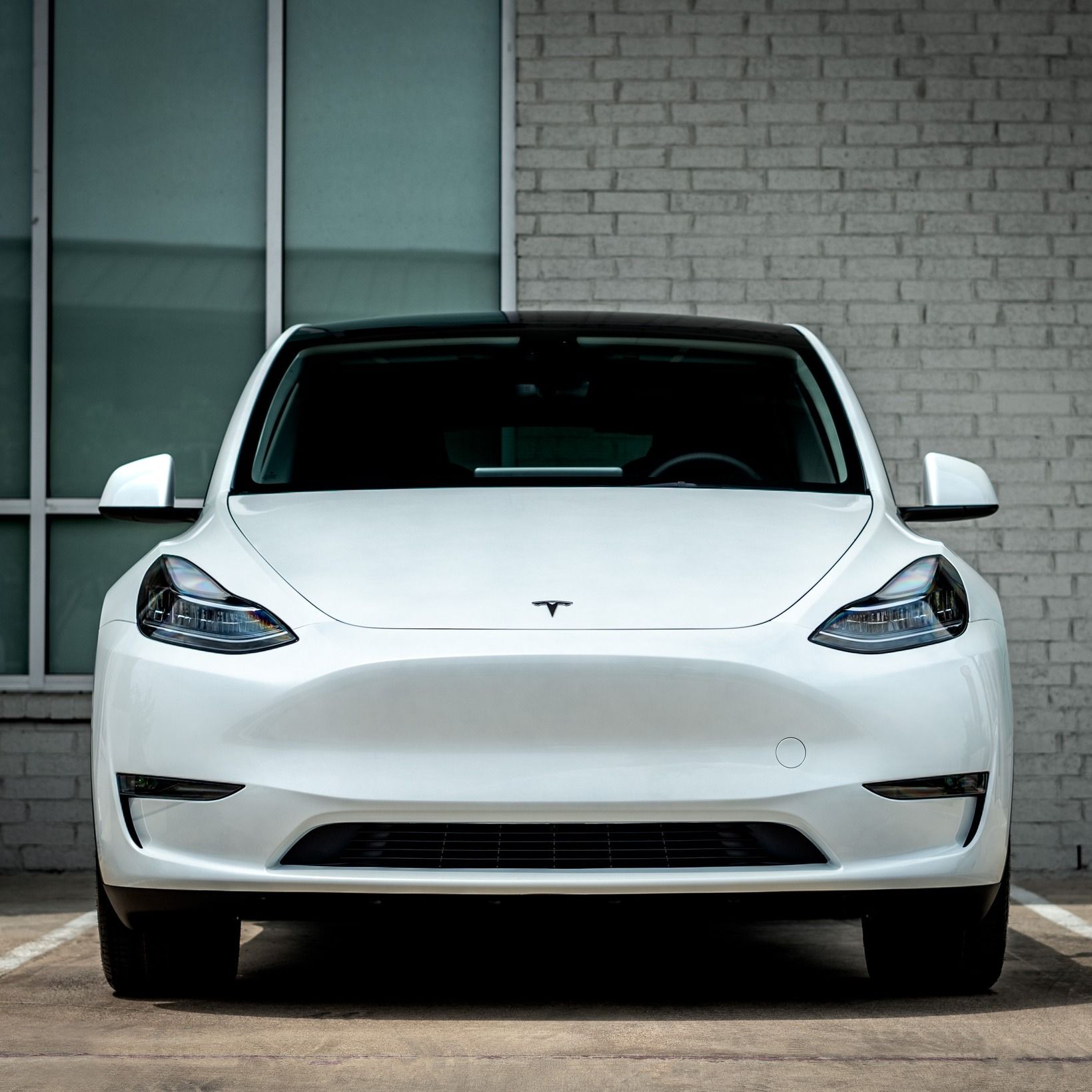 A white tesla model y is parked in front of a brick building.