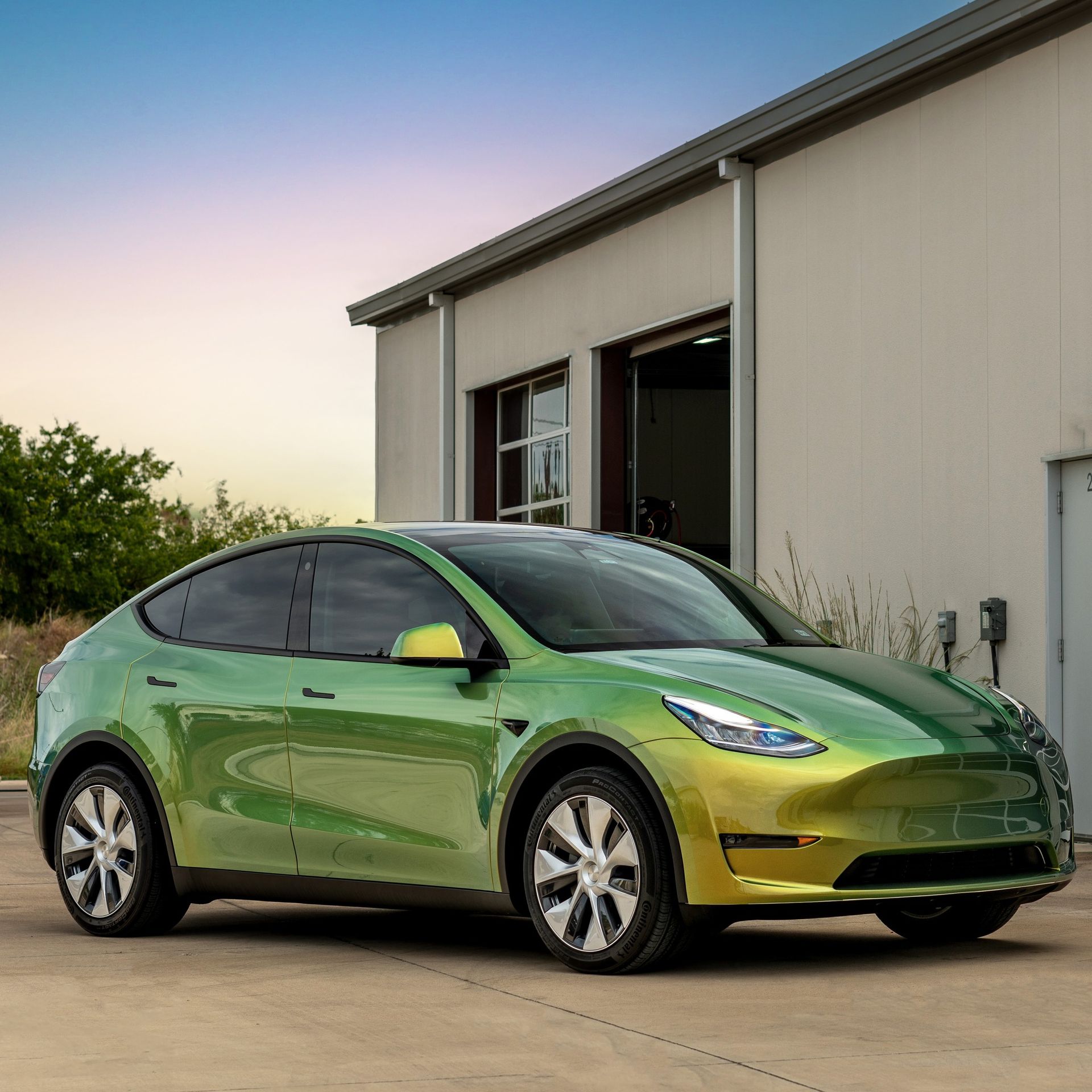 A green and yellow tesla model y is parked in front of a building.