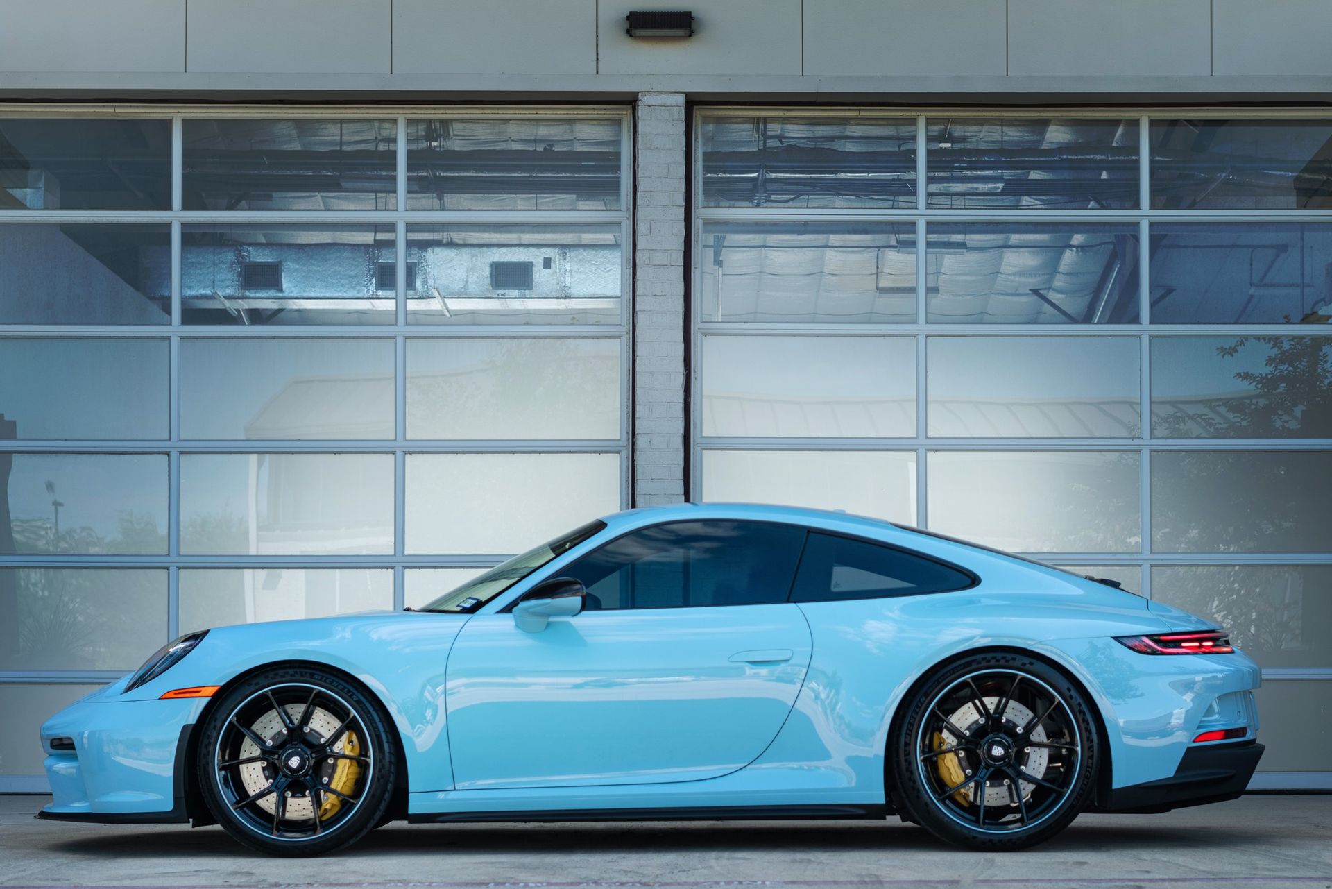 Light blue Porsche sports car parked in front of a garage.